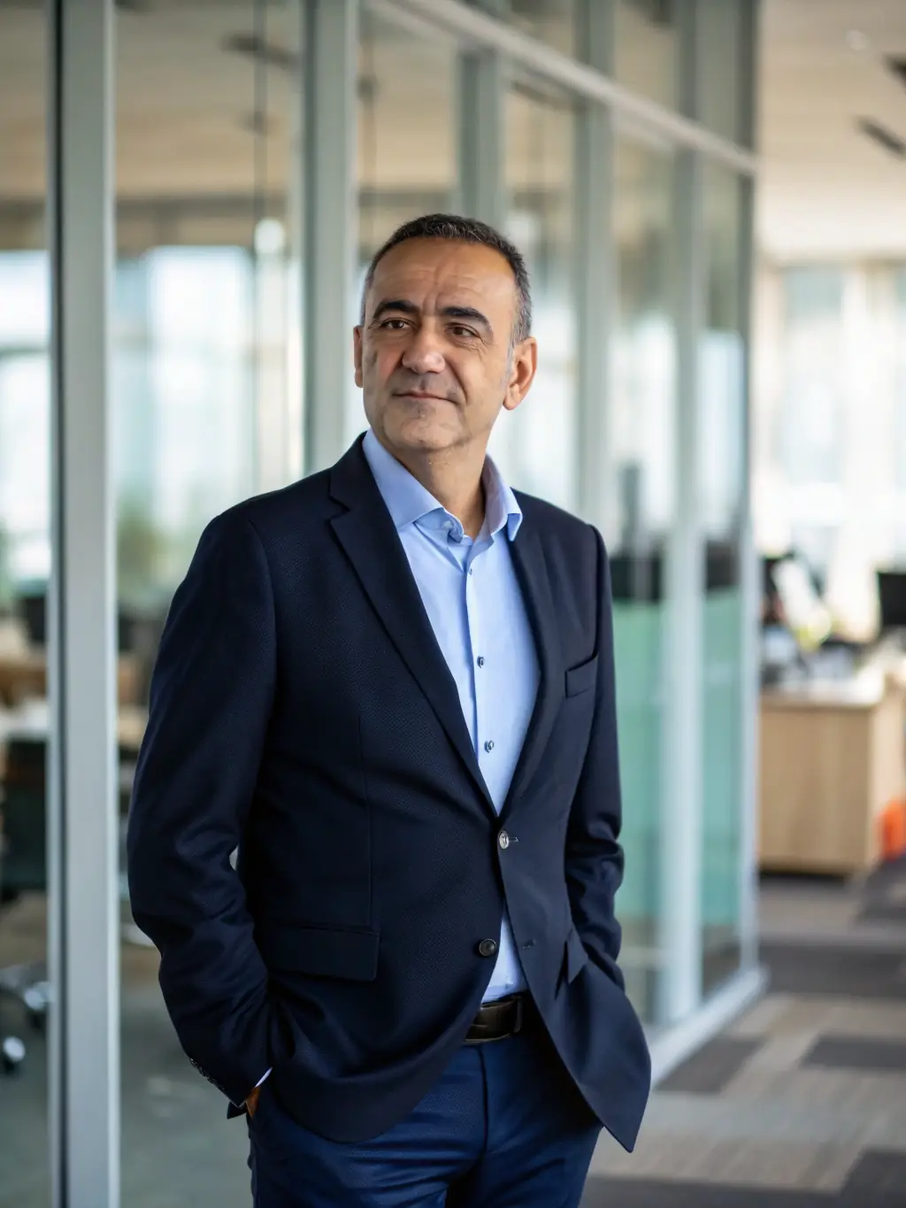 A professional headshot of a keynote speaker at a past procure.uno conference, smiling confidently and looking directly at the camera. The background is a blurred conference hall.