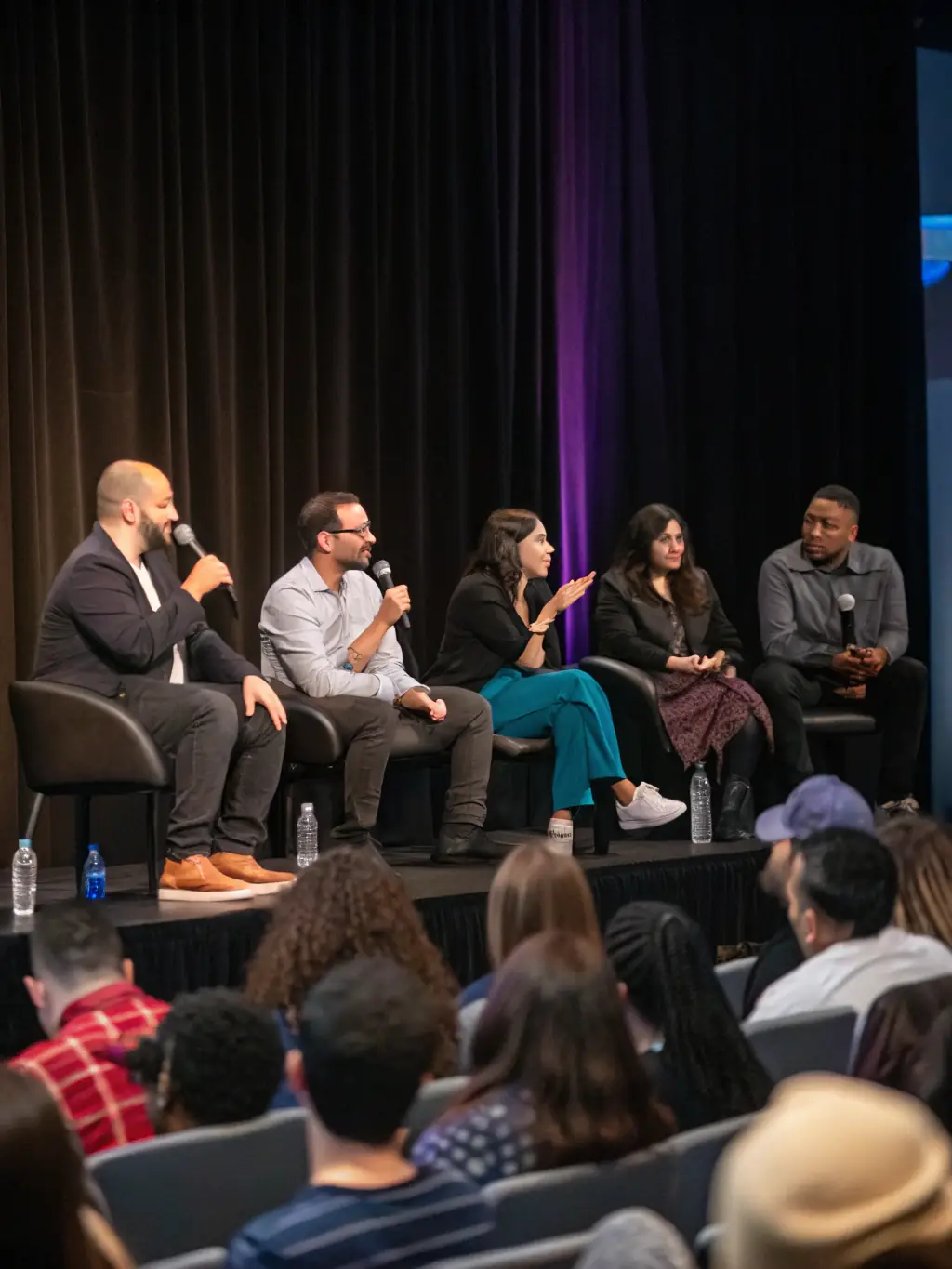 A photo of a panel discussion at a procure.uno conference, featuring four panelists engaged in a lively debate. The audience is visible in the background, listening attentively.